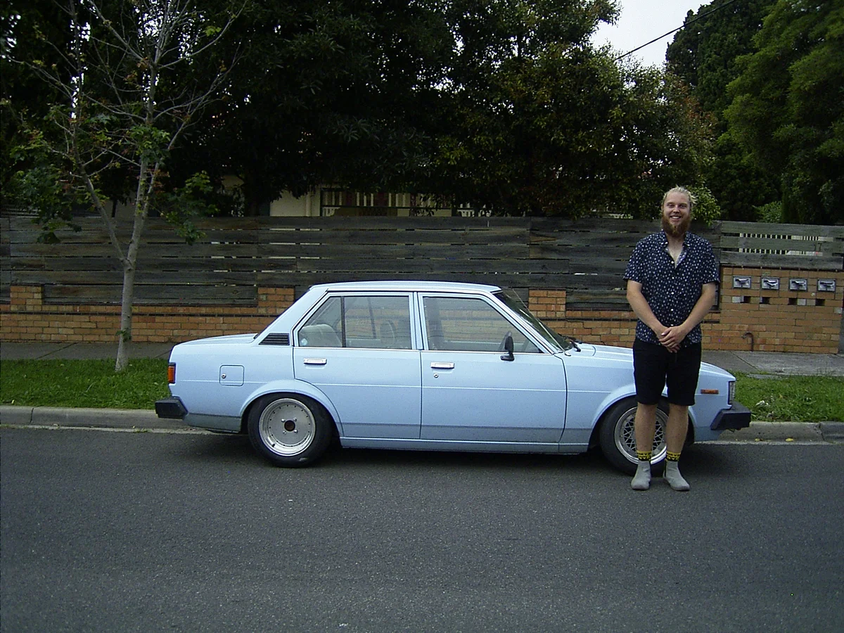 Cameron standing beside a light-blue car.